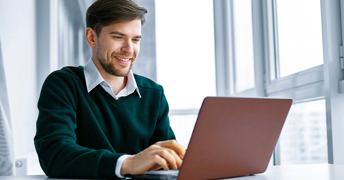 A man smiling while using a laptop