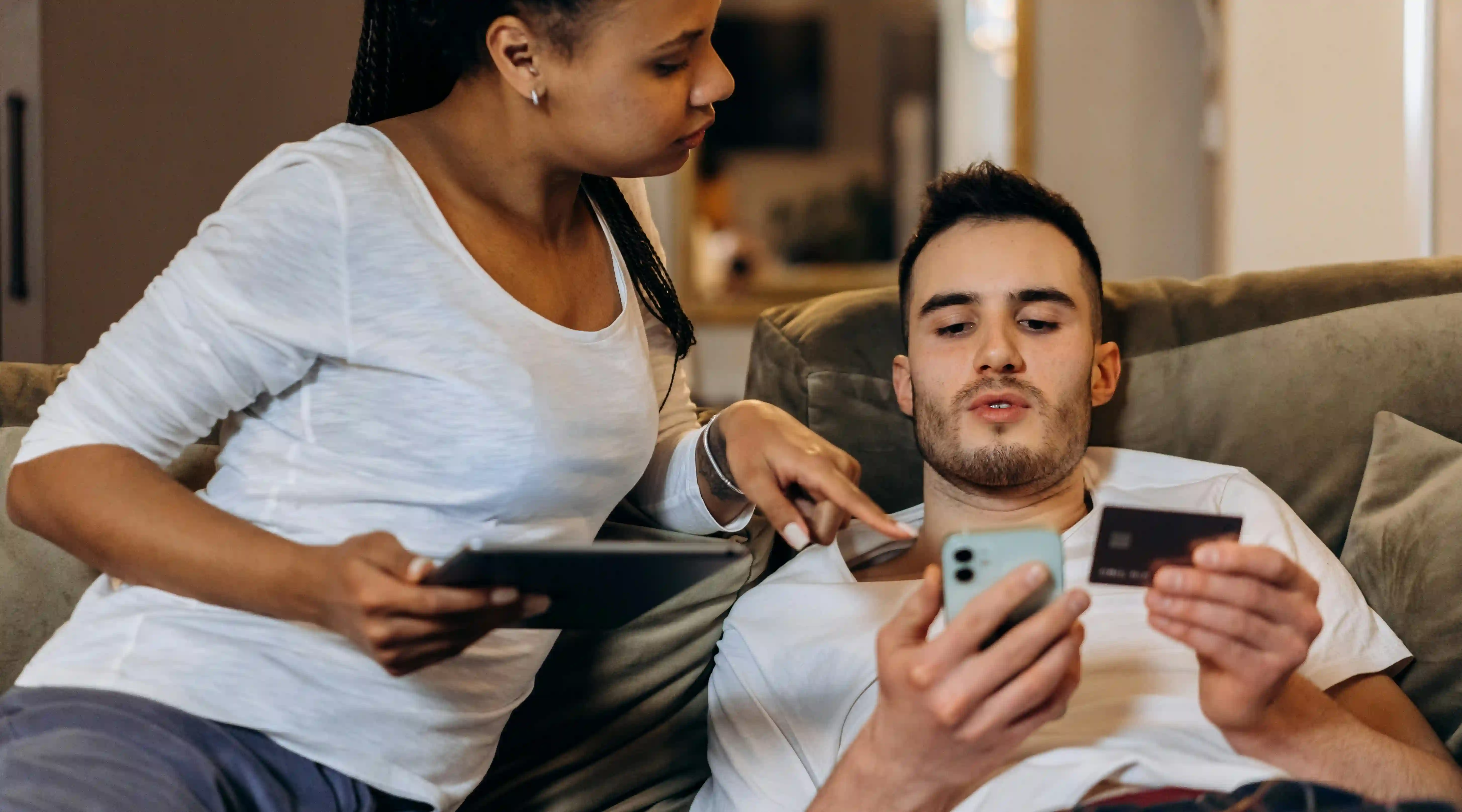 A woman informing a man about con artist scams while he checks his phone and his credit card