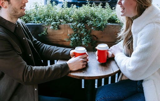 A man and a woman sitting together and holding identical takeaway cups