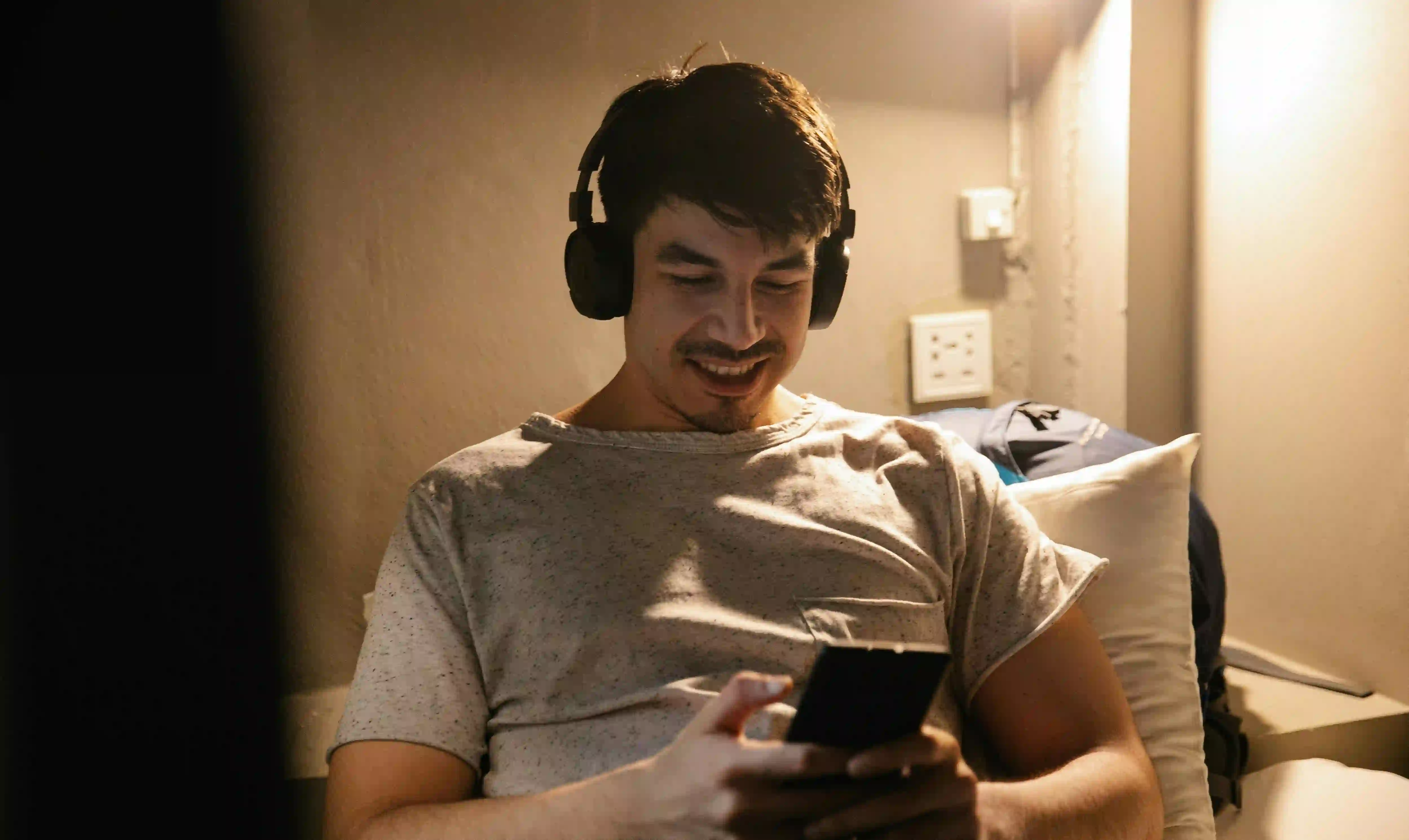 A man with black headphones smiling while looking at his phone and listening to some good breakup music