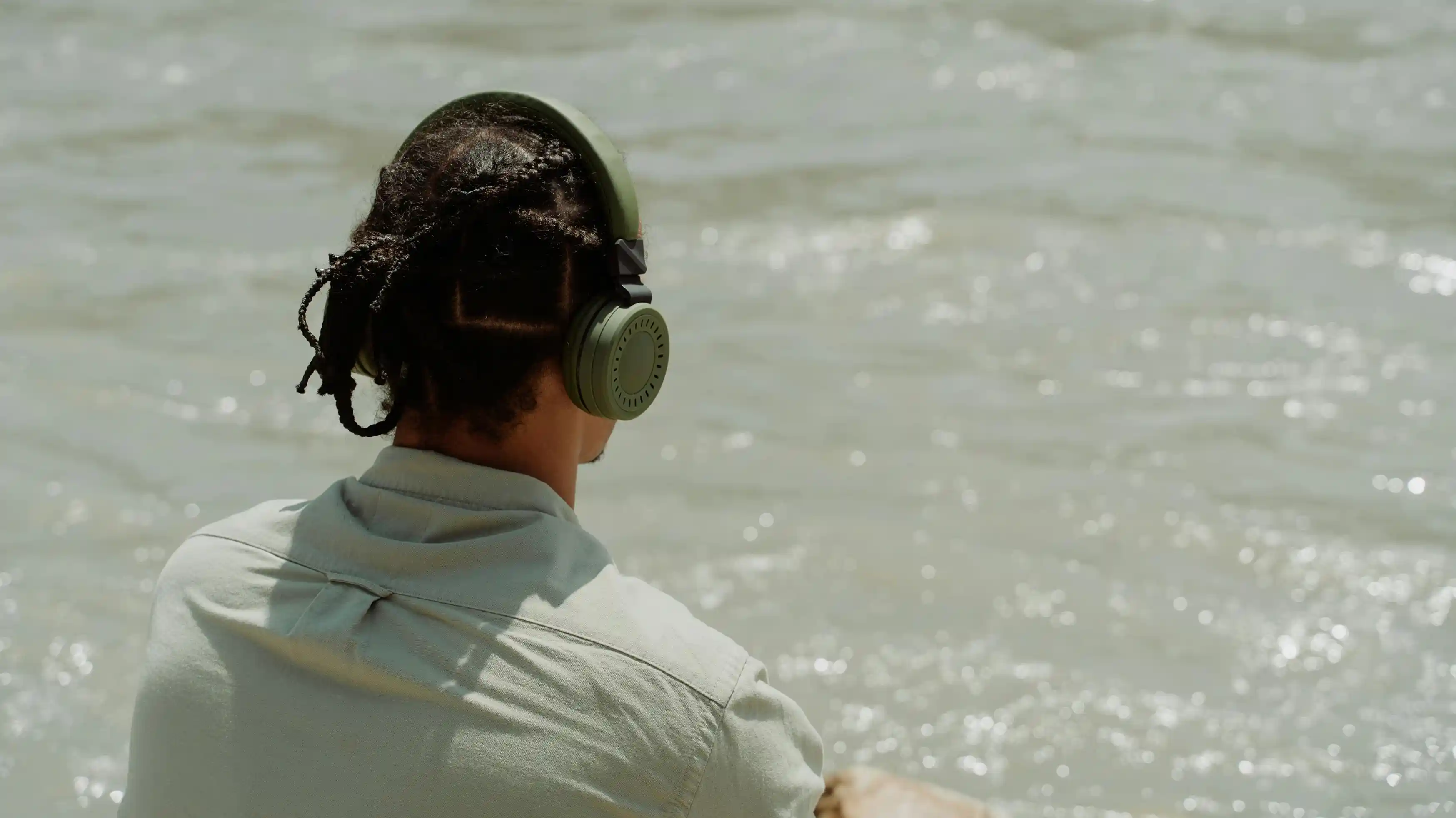 A man with green headphones listening to heartbreak songs facing the sea