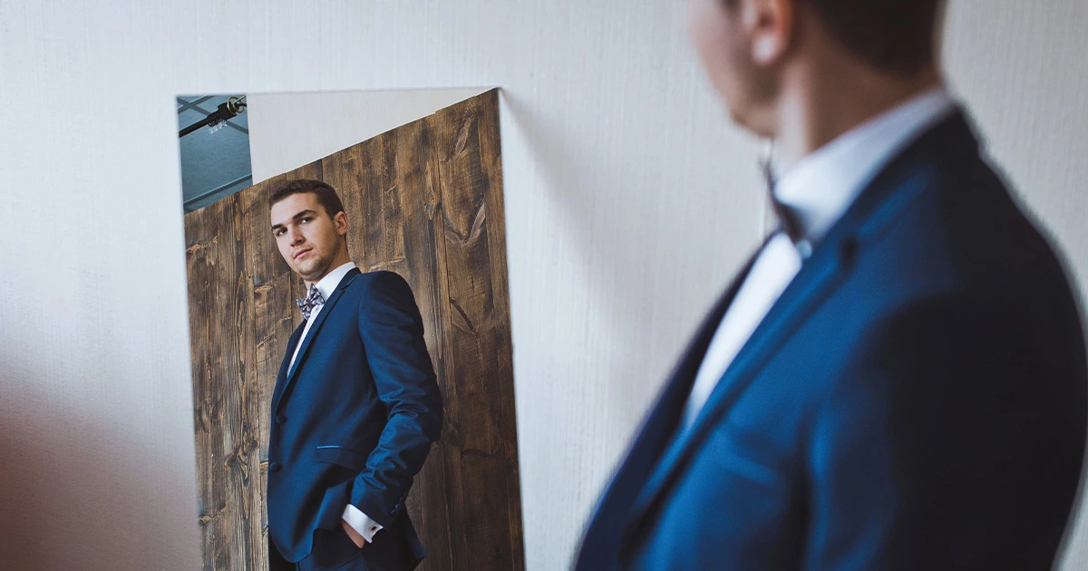 A man in a blue suit looking at himself in the mirror