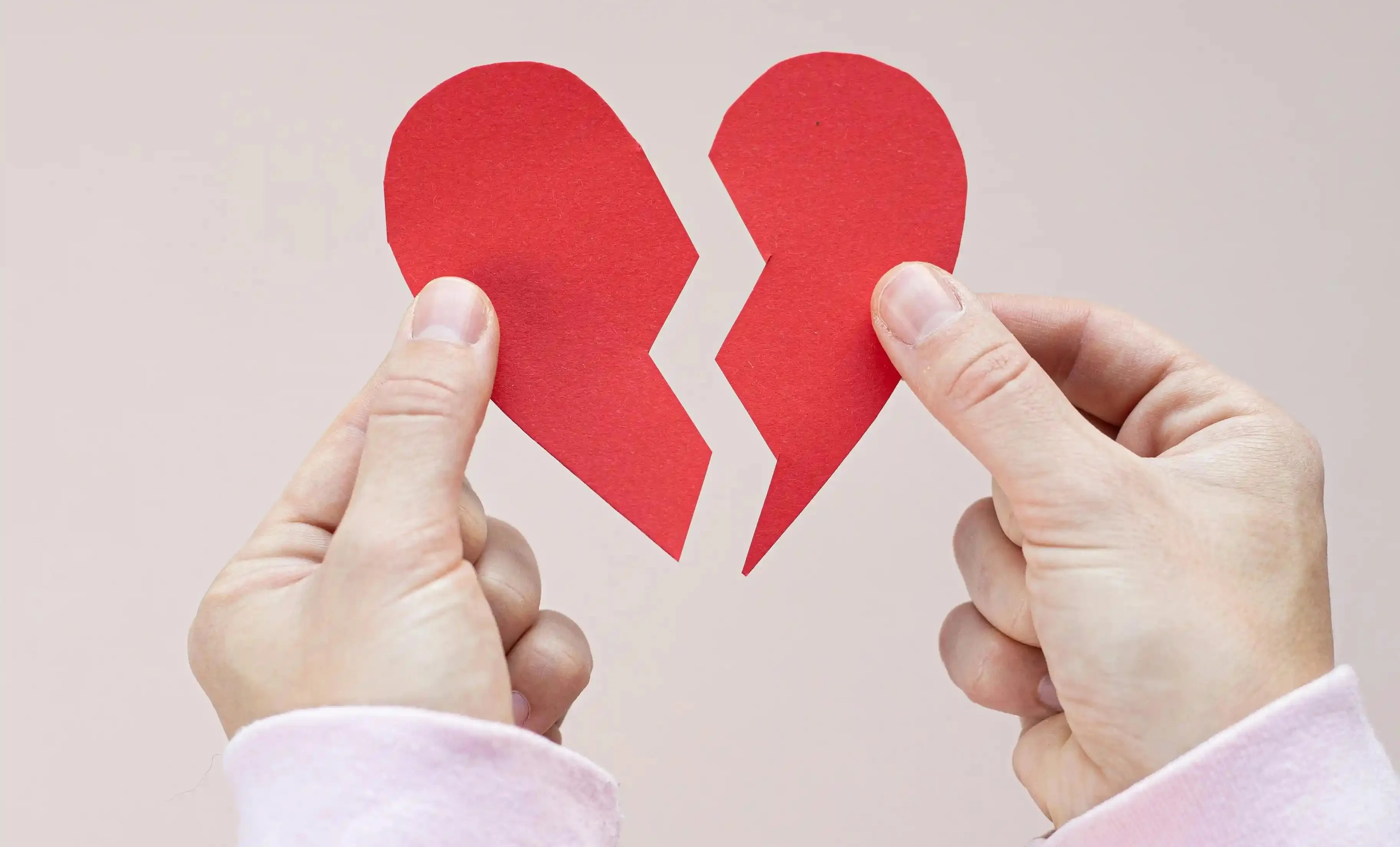 A person holding two halves of a broken paper heart