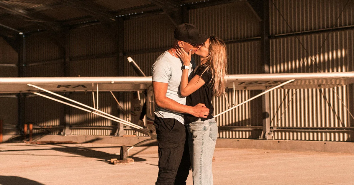 A man and his partner kissing in front of a plane in an act of building intimacy that is helpful for those who want to learn how to make a long-distance relationship work