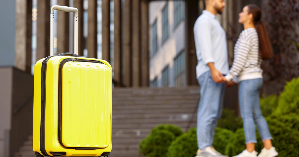 A couple holding hands near a yellow luggage