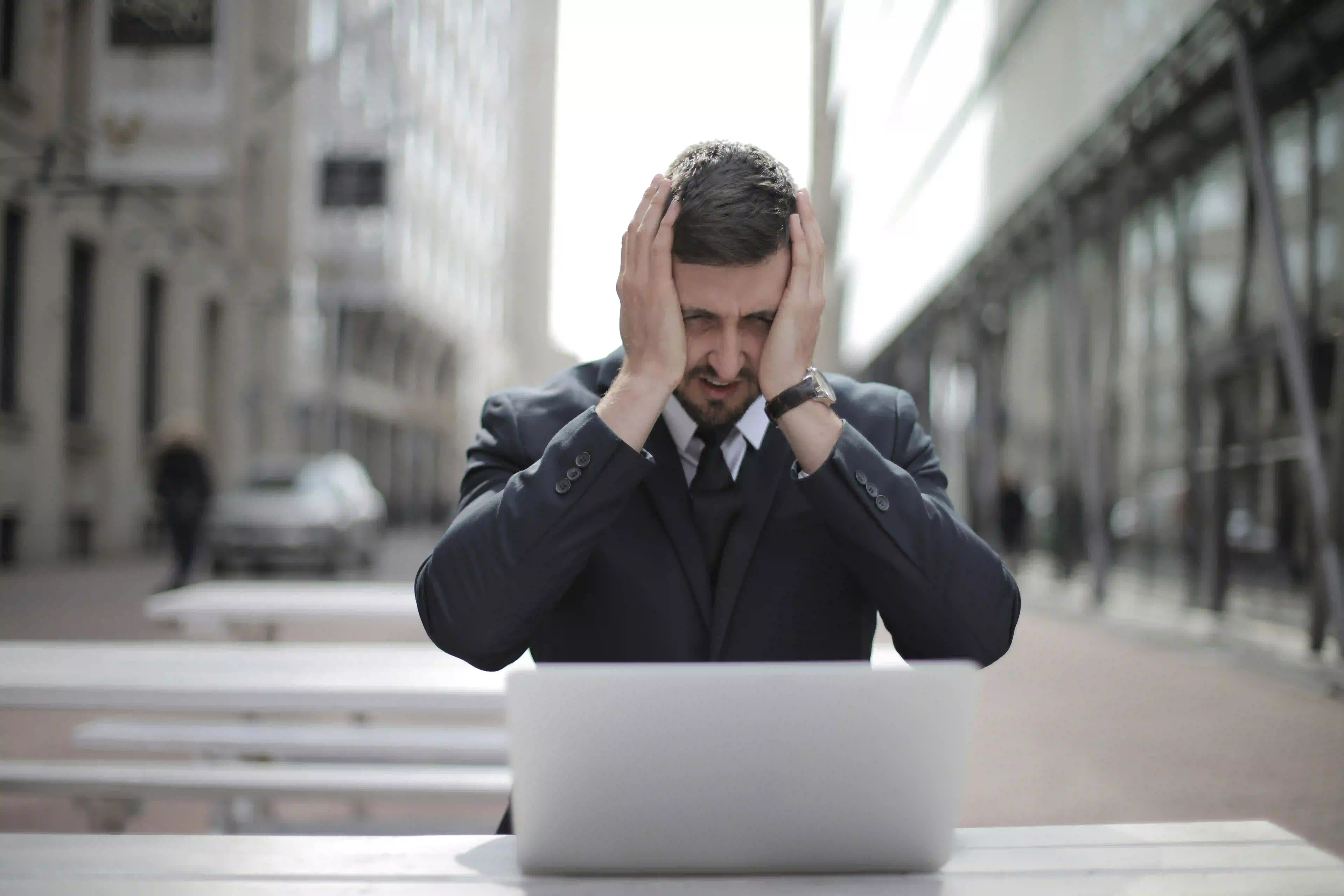 A man with his hands on his head while facing a laptop