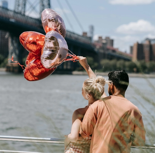 A couple spending time together by the bay while the lady is happily holding out heart balloons is an example of an ideal first date