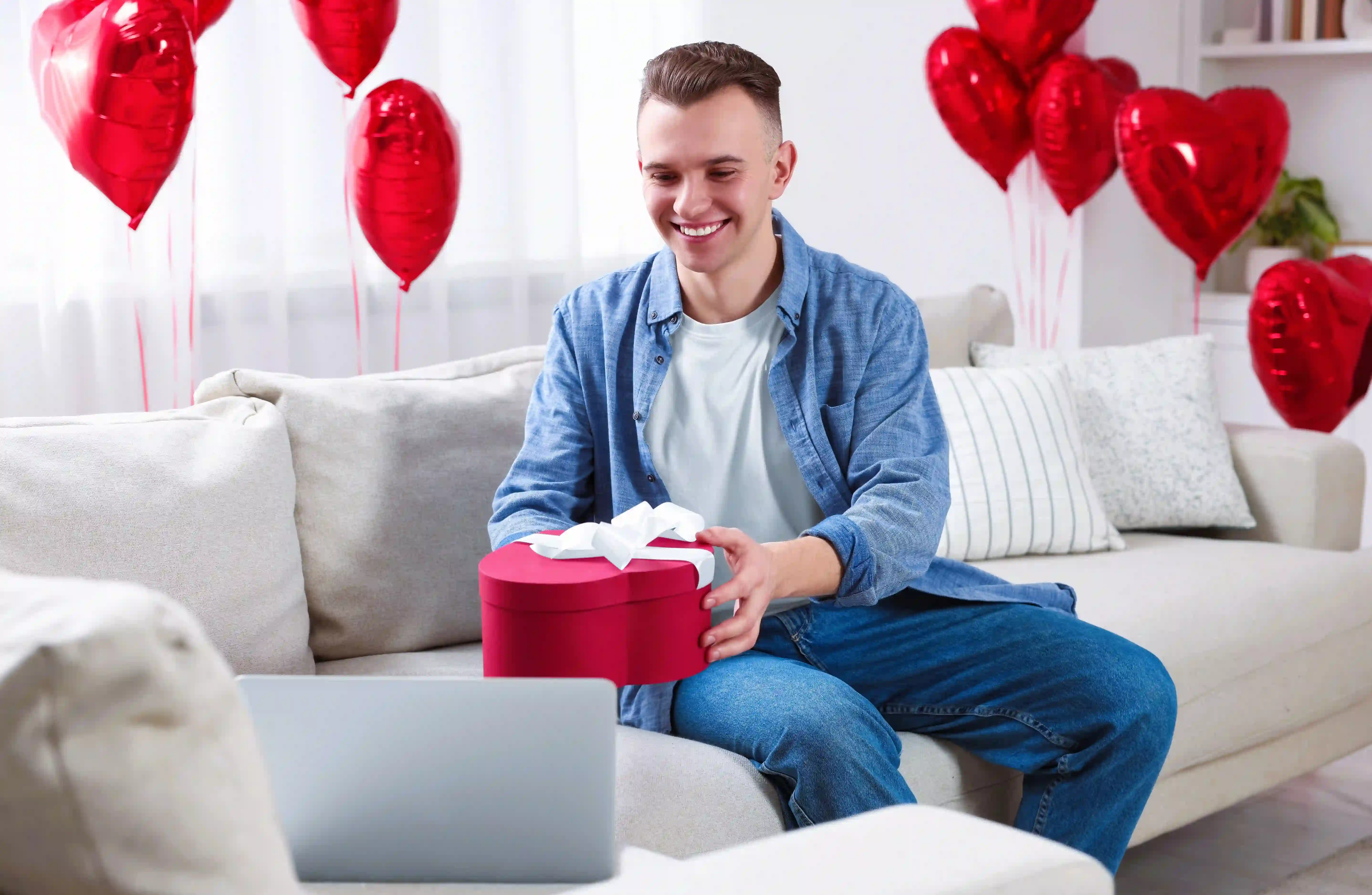 A man giving a heart-shaped Valentines gift to someone he’s talking to on his laptop