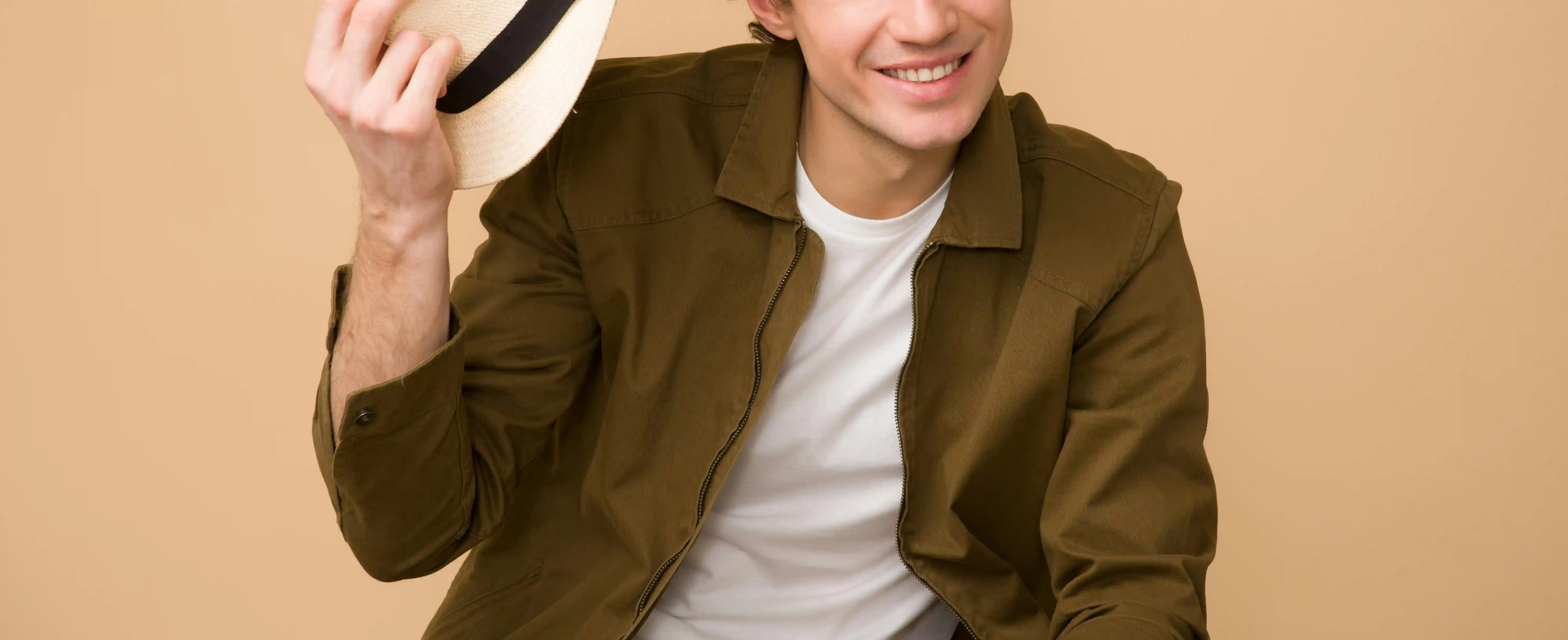 A man wearing a plain white shirt under an olive green jacket with a black and white fedora hat is an example of good mens date night outfits