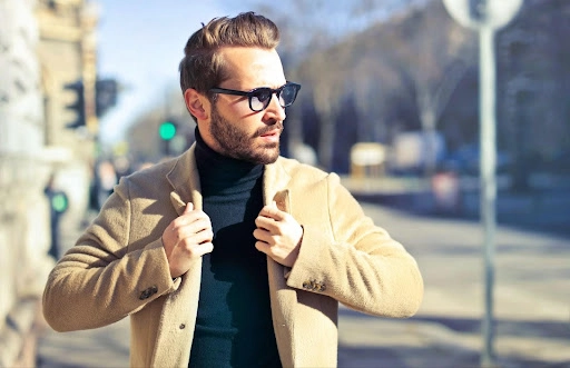 A man wearing dark sunglasses and a light brown coat