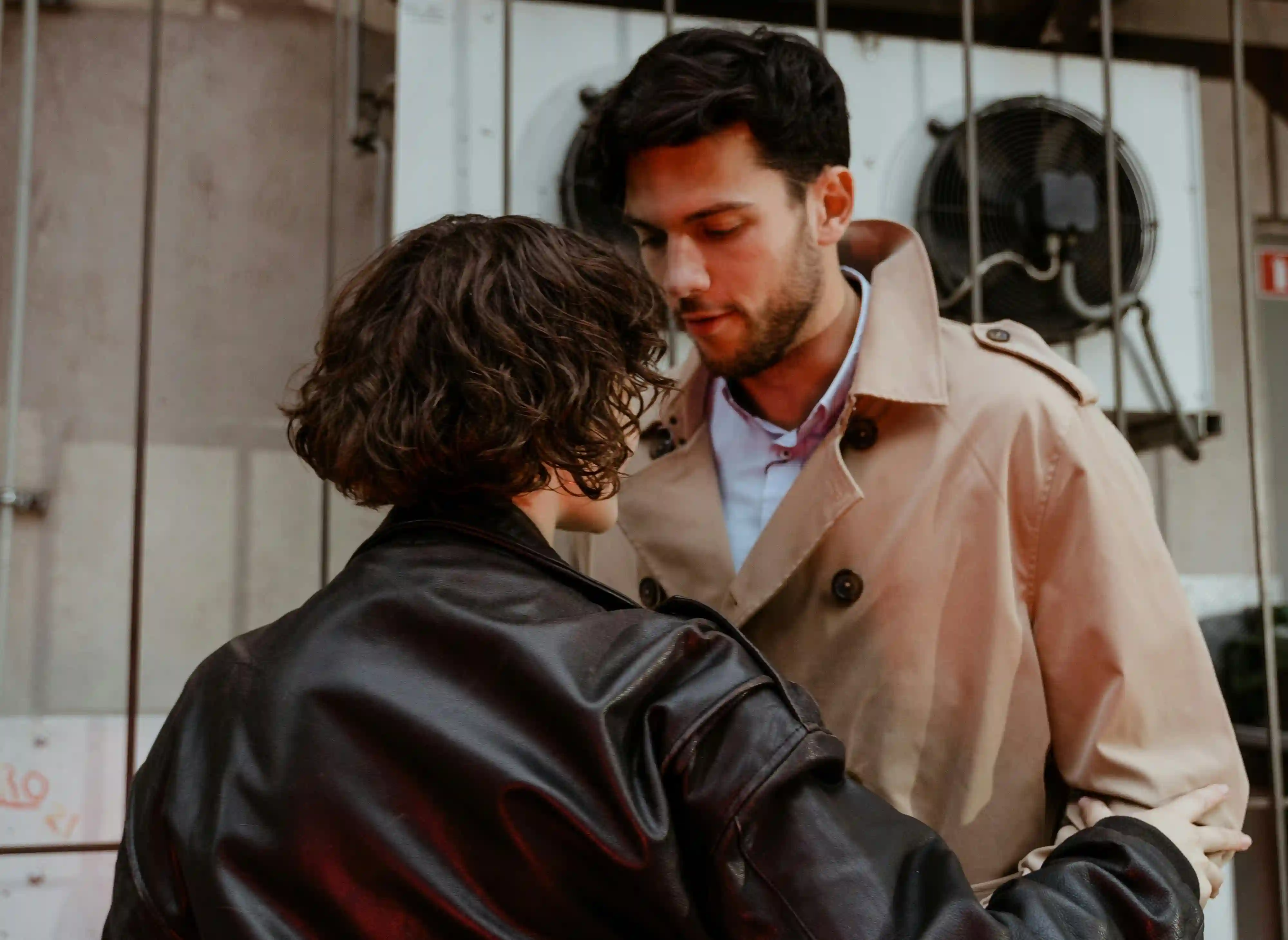  A man in a brown coat staring down at a woman in a black leather jacket